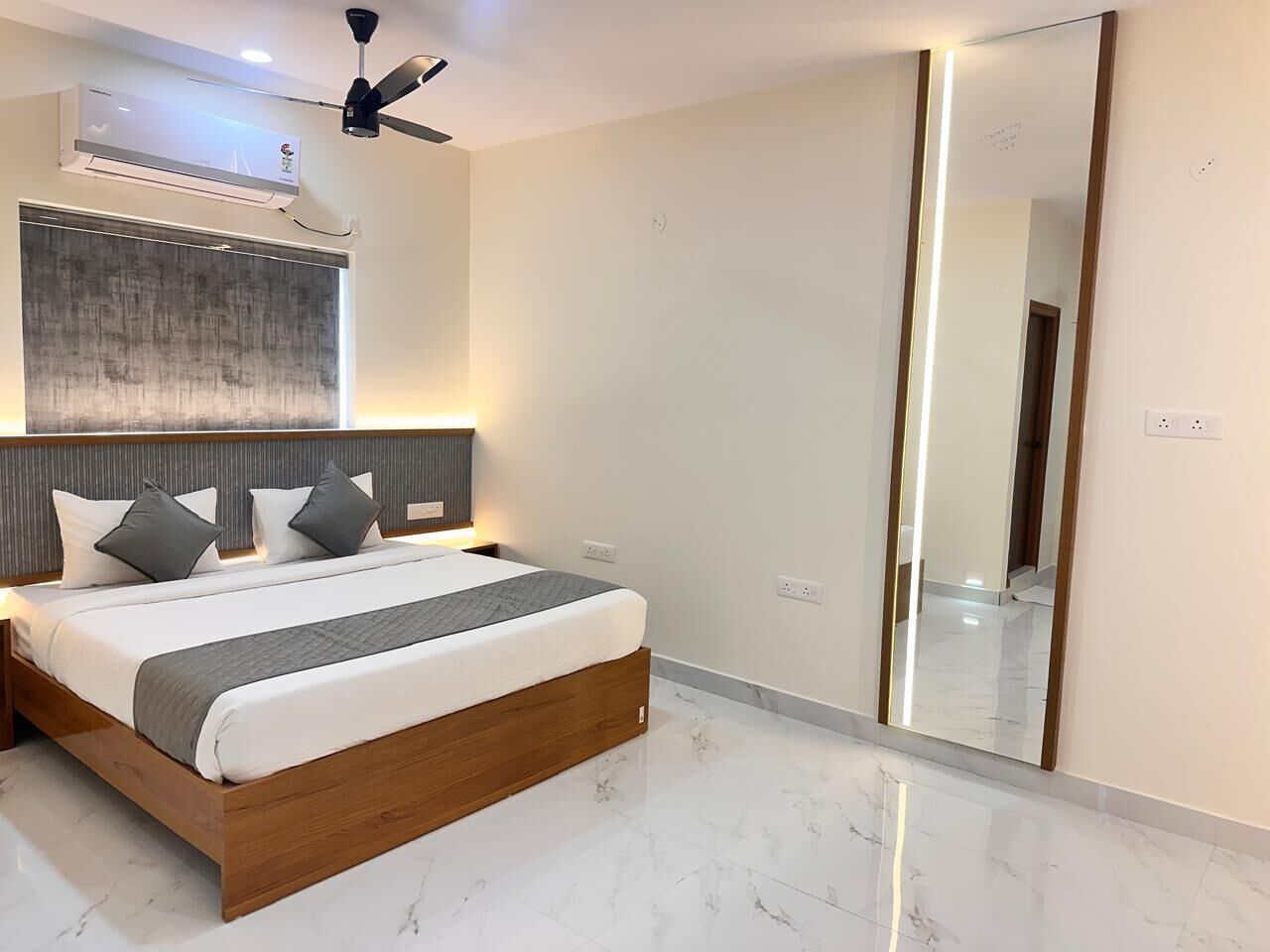 A modern bedroom with a large bed, a ceiling fan, an air conditioning unit, and a large mirror.