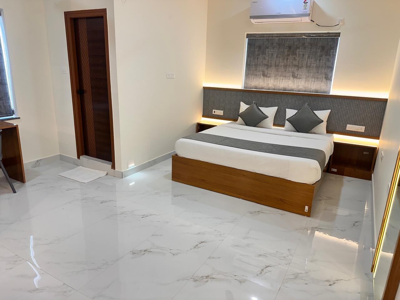 A modern bedroom with a large bed, marble flooring, and a wooden door.