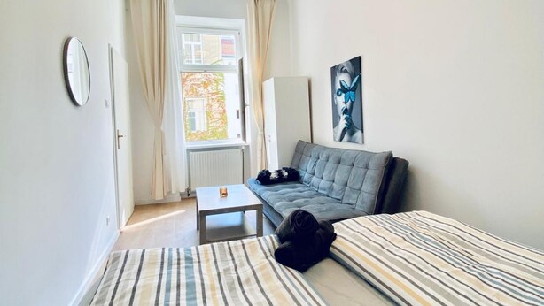 A room with a bed, a sofa, a small table, a mirror, and a window with curtains.