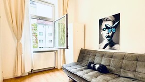 A room with a sofa, a window with curtains, and a wall-mounted artwork.