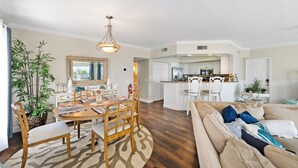 A spacious living room with a large beige sofa, a wooden dining table with chairs, and a kitchen area in the background. - Updated Spacious condo with Coastal Decor across from beach with peeks of Gulf (Bradenton Beach)