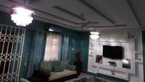 Una sala de estar con un sofá, un televisor montado en la pared, un ventilador de techo e iluminación decorativa.