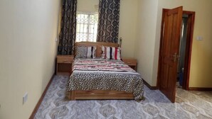 Un dormitorio con cama, cortinas, una puerta de madera y suelo estampado.