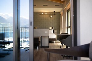 A modern hotel room with a bed, bedside table, and a view of boats through large windows. - Lago Dorato Marina Lodge - Lakefront  (Colico)