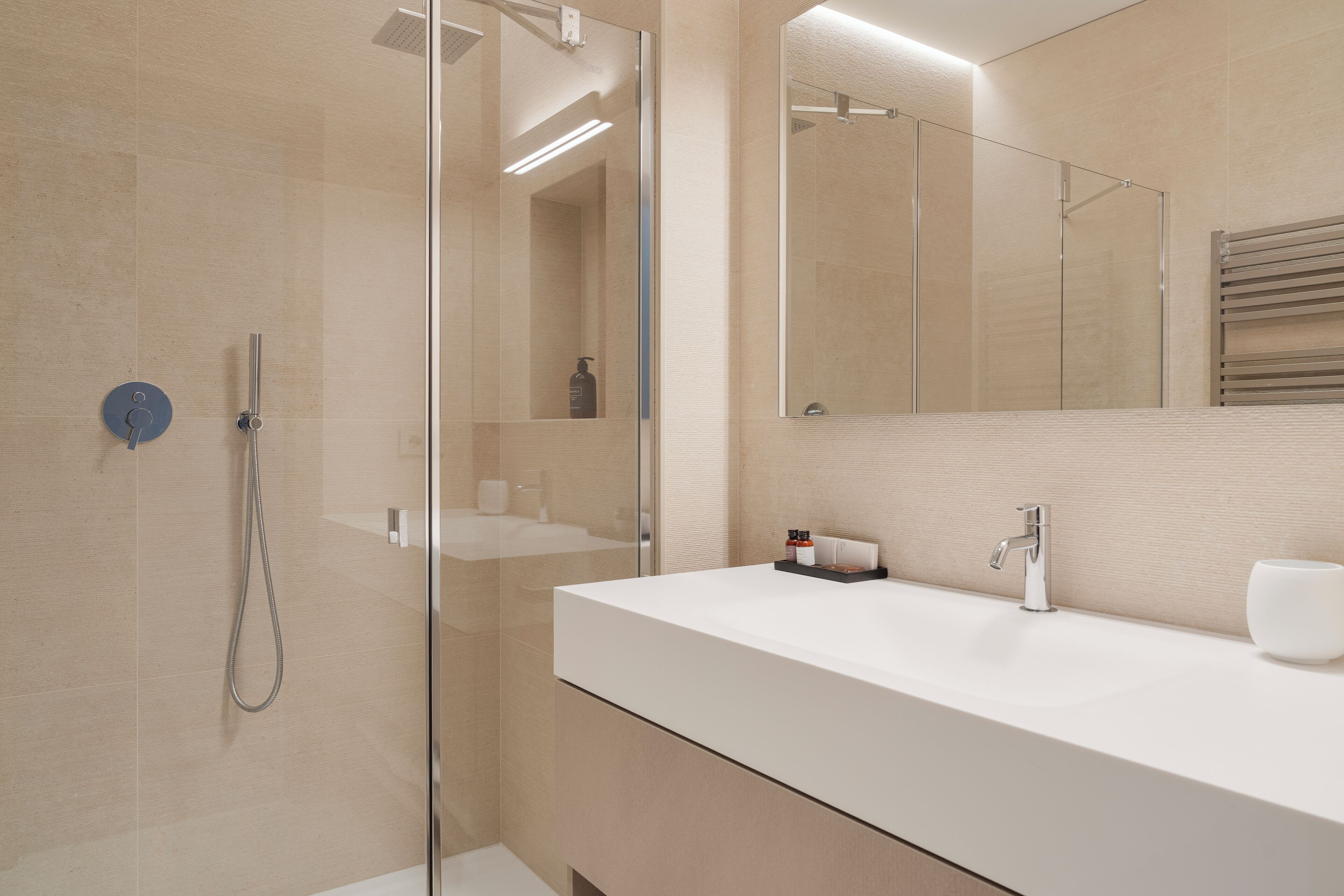 Une salle de bain moderne avec une douche à parois de verre, un lavabo blanc et un grand miroir.