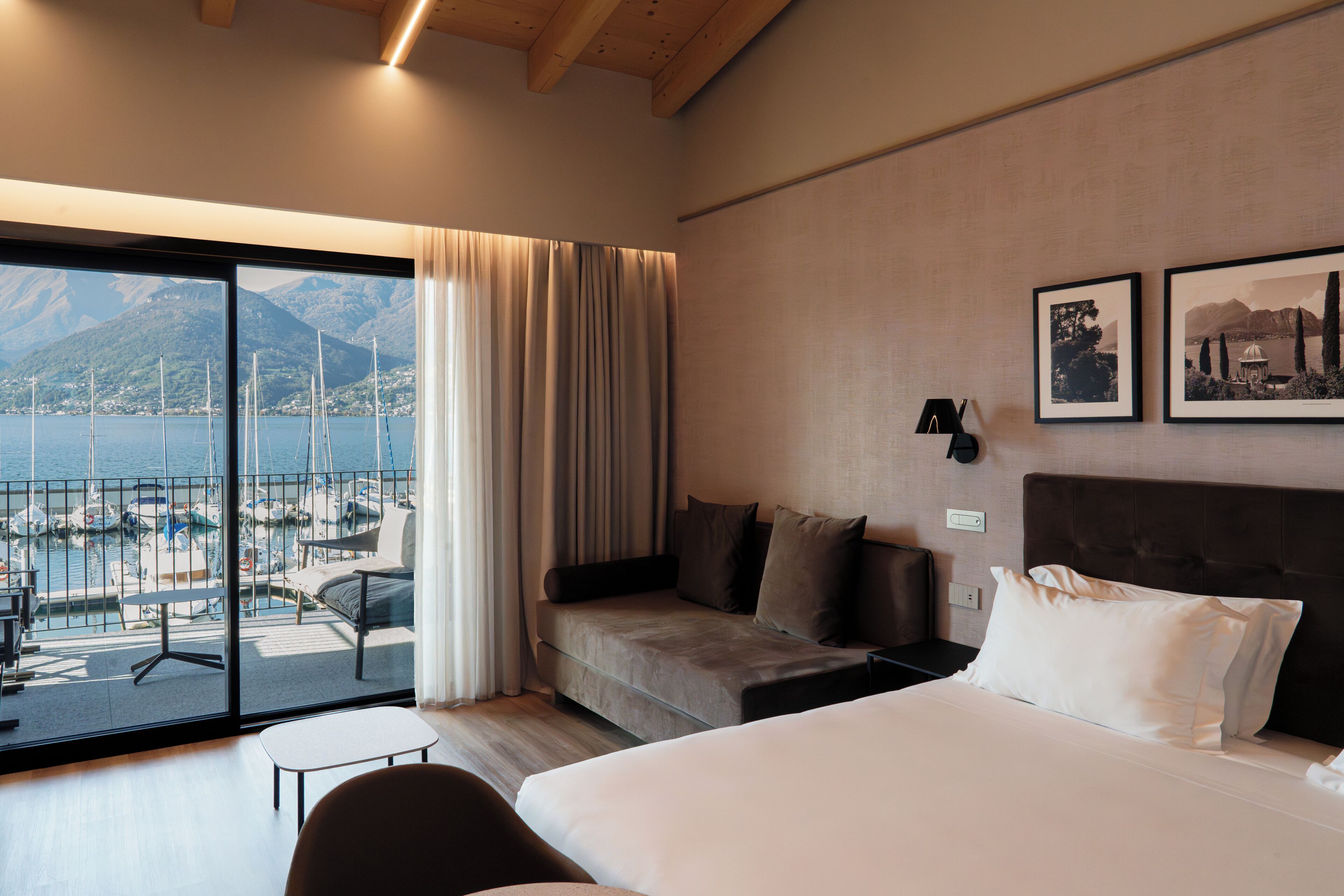 Una camera d'albergo con un letto grande, un divano, un tavolino e vista su un porto turistico con barche.