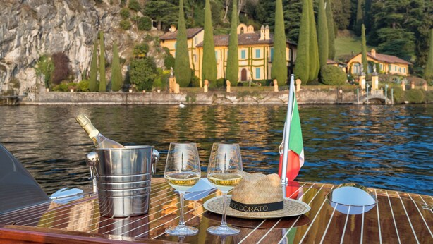 Un bateau avec une bouteille de champagne, deux verres à vin, un chapeau de paille et un petit drapeau italien sur le pont.
