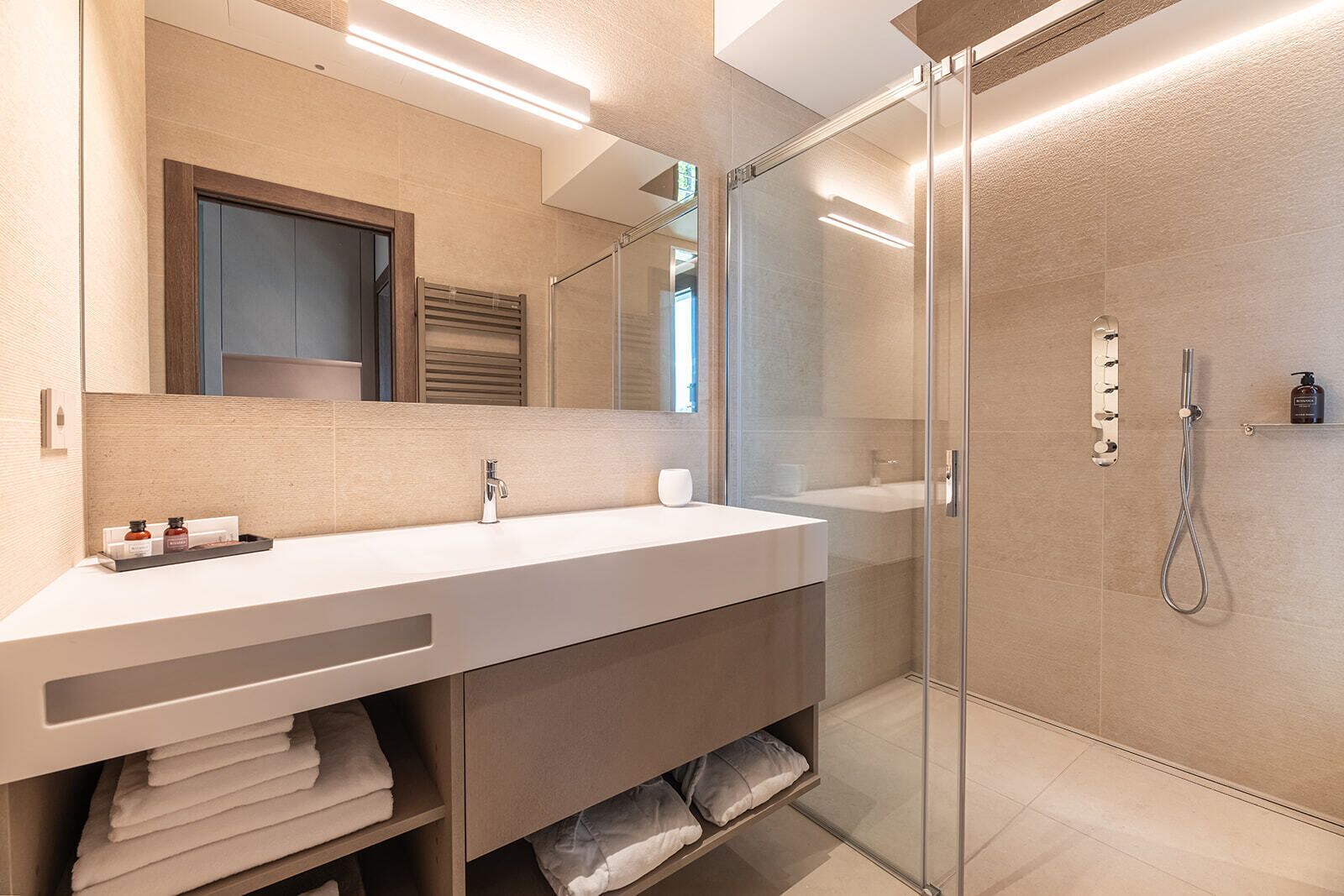 A modern bathroom with a glass-enclosed shower, a large mirror, and a vanity with a towel rack.