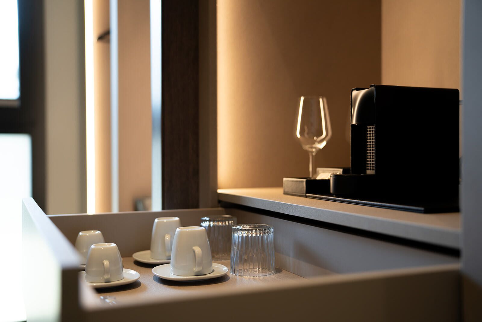 A coffee station with cups and a glass, and a coffee machine on a counter.