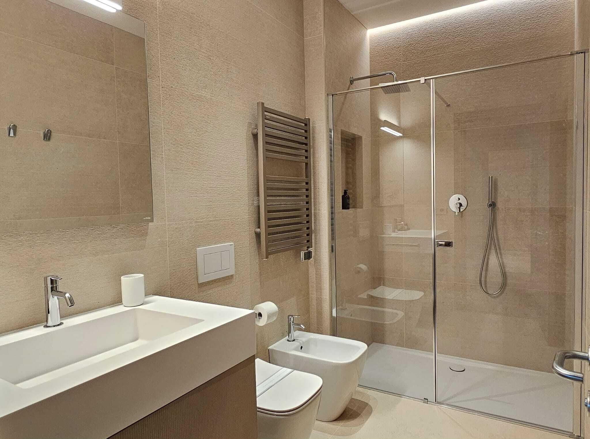 Un baño moderno con un lavamanos grande, inodoro, bidé y zona de ducha con mampara de cristal.