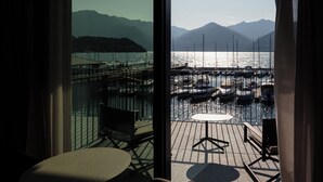 Un balcon avec une table et des chaises, donnant sur une marina où sont amarrés des bateaux, avec des montagnes en arrière-plan.