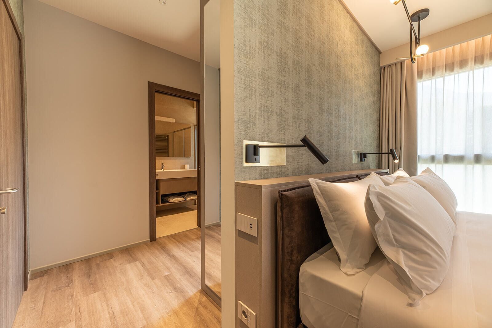 A modern hotel room with a bed, bedside table, and a large mirror.