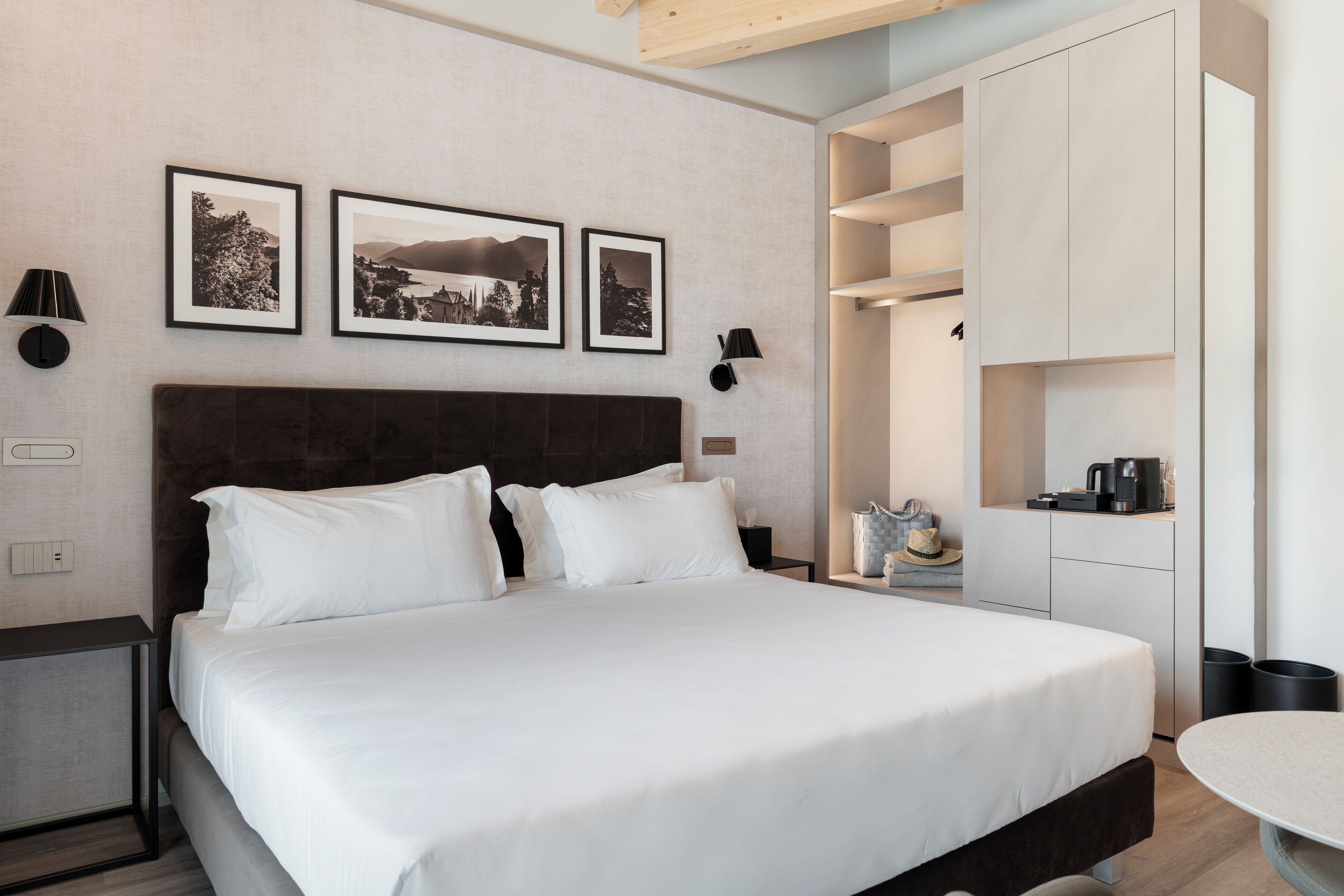 Ein modernes Hotelzimmer mit einem großen Bett, einem Nachttisch, einer Lampe und einem an der Wand befestigten Regal mit einer Kaffeemaschine.