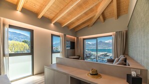 Une chambre d’hôtel moderne dotée d’un grand balcon, de poutres apparentes en bois au plafond et offrant une vue sur un paysage montagneux.