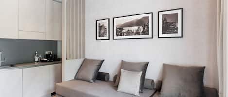 A modern living space with a sofa, a kitchen area, and three framed pictures on the wall.