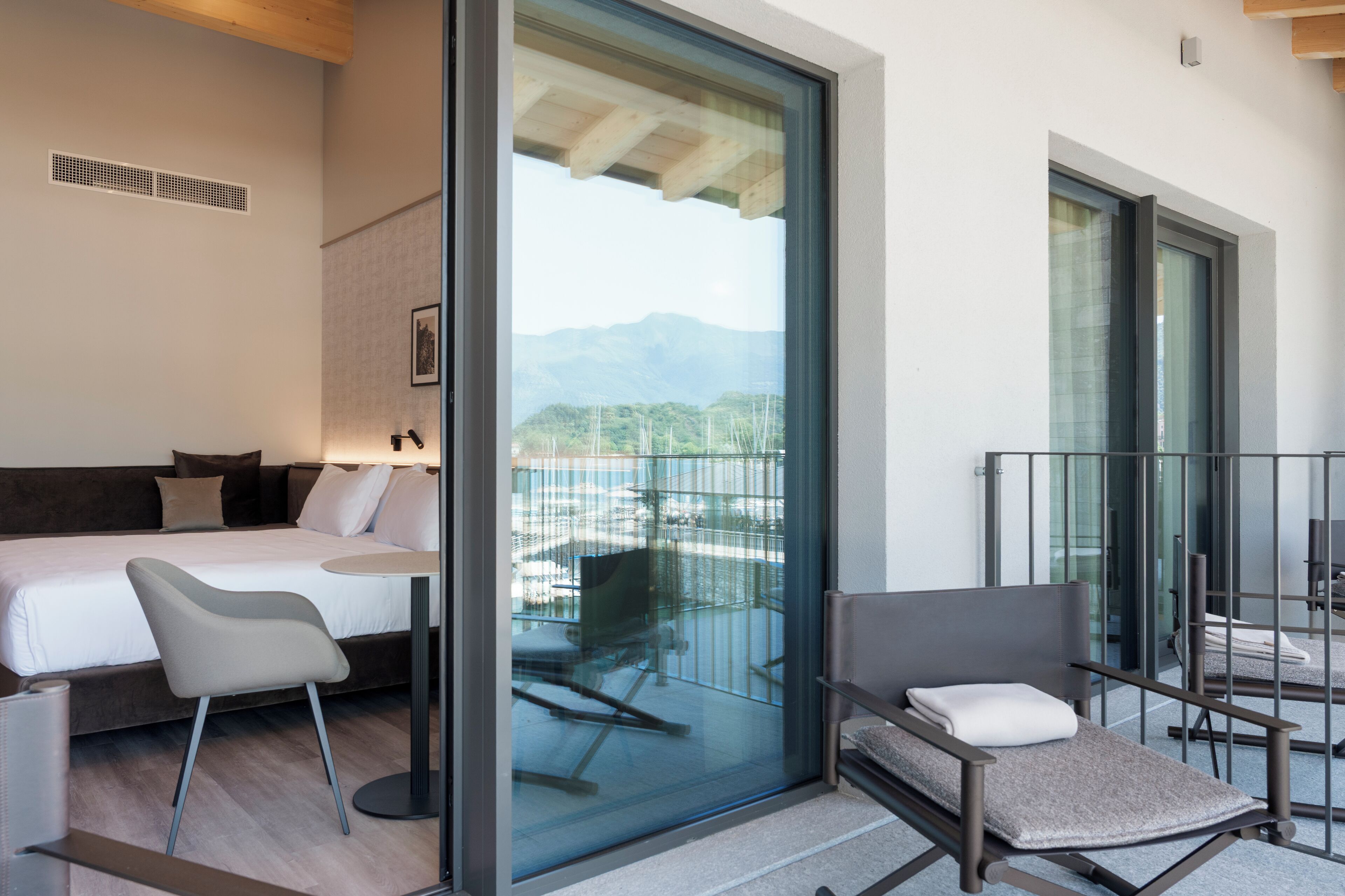 A modern hotel room with a bed, a desk, and a balcony with a view of mountains.