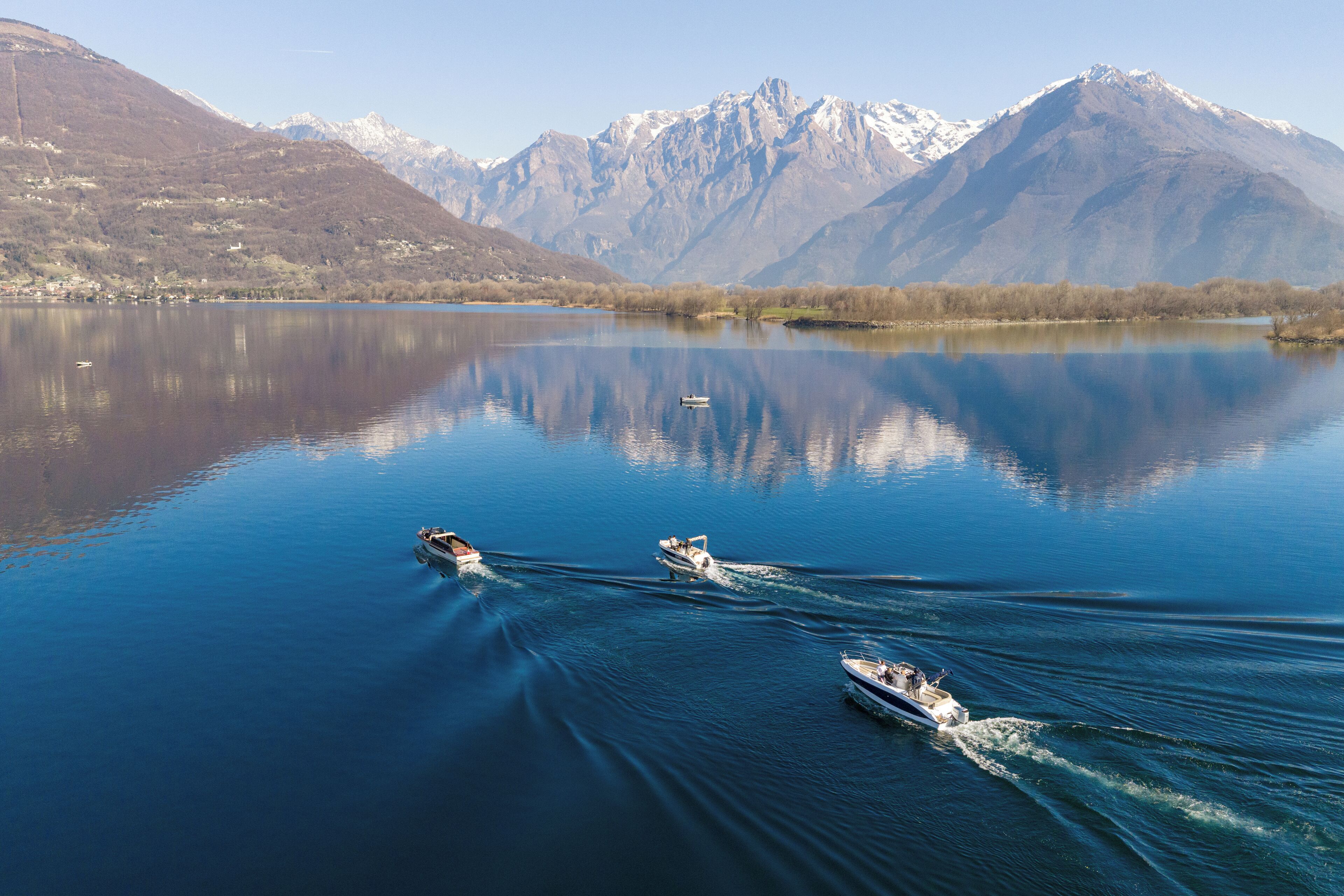 Un lago tranquilo con barcos, montañas al fondo y cielos despejados.