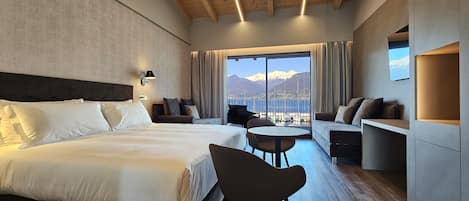 A hotel room with a large bed, a seating area with a table, and a view of mountains through large windows.