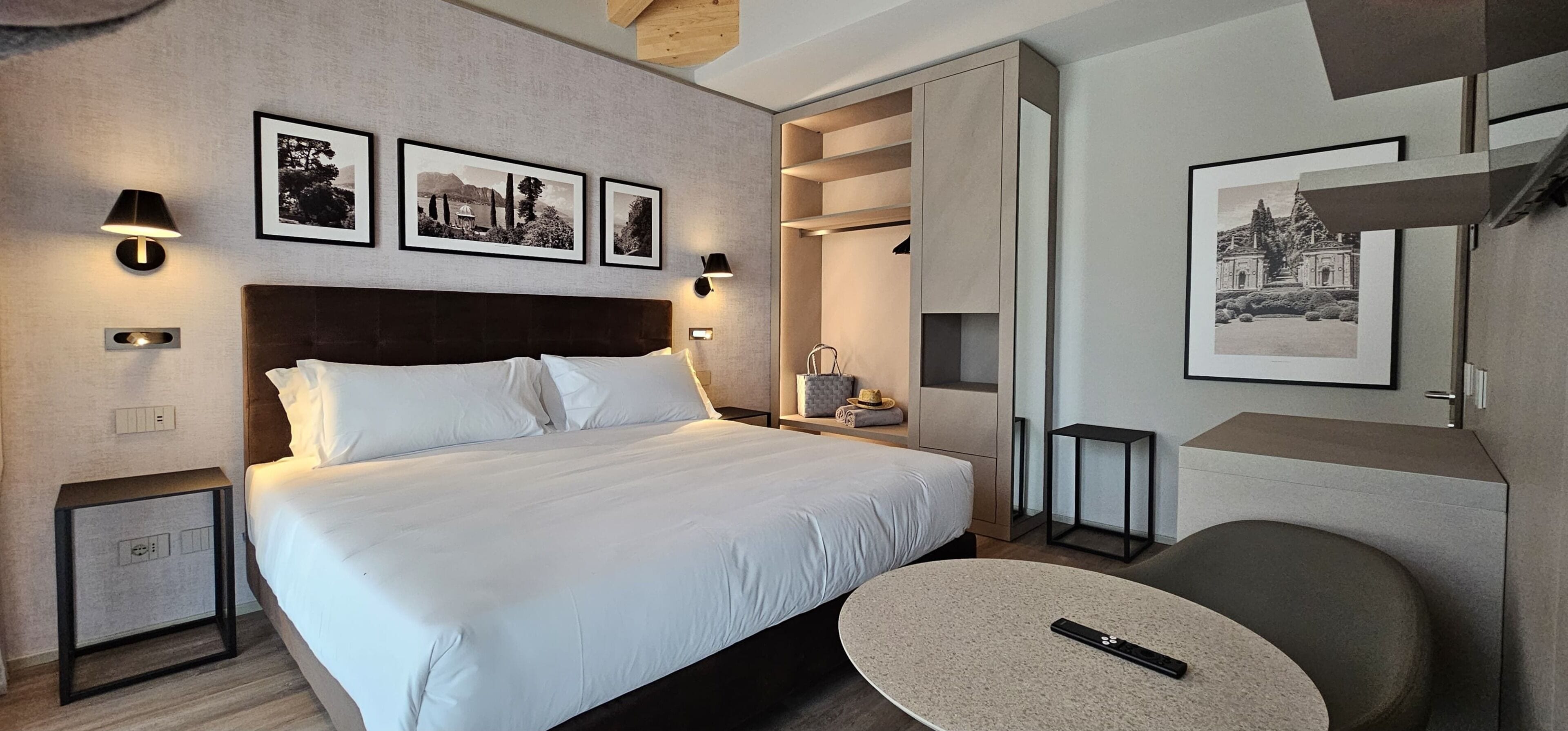 A hotel room with a large bed, bedside tables, a chair, a small table, and artwork on the walls.