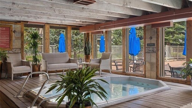 Un espace piscine extérieur abrité, doté de chaises longues, d’un jacuzzi et de parasols.