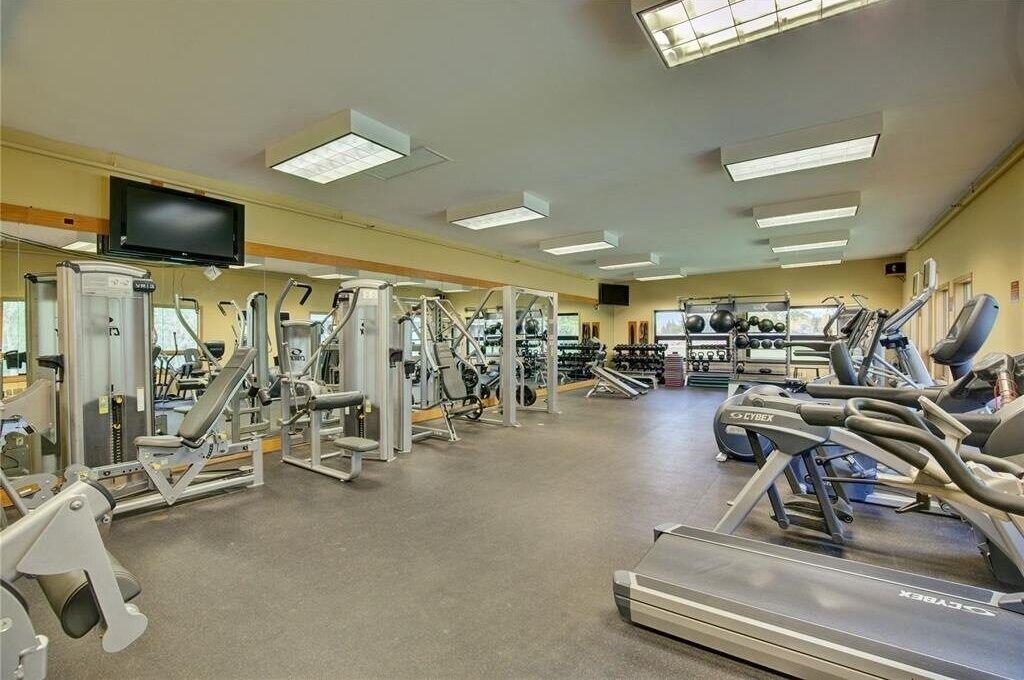 Une salle de sport équipée de divers appareils d’exercice, d’un tapis de course et d’un téléviseur fixé au mur.
