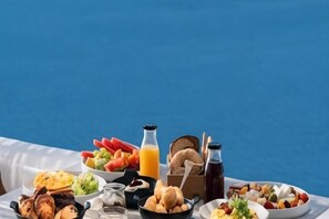 A table with various food items and drinks, set against a blue background. - Volcano View Hotel Santorini (Santorini)