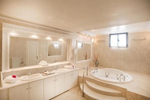 A modern bathroom with a large mirror, two sinks, a bathtub, and a window. - Volcano View Hotel Santorini (Santorini)