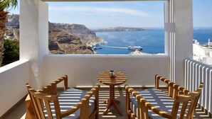 Un balcon offrant une vue sur les falaises et la mer, des chaises en bois, une petite table ronde et une balustrade blanche.