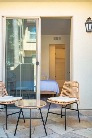 A room with a glass door leading to a balcony with wicker chairs and a small round table. - Private Entry Suite w Patio Bath Kitchenette (Lake Forest)