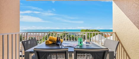 A balcony with a table and chairs, a view of the sea, and a building in the background.
