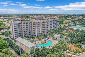 A multi-story hotel with a central pool surrounded by palm trees and lounge areas.