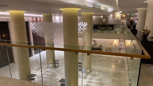 En rummelig lobby med marmorgulv, høje søjler og gelænder af glas.