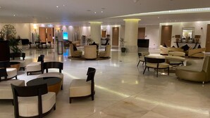 En rummelig lobby med flere siddeområder, herunder sofaer og stole, arrangeret omkring et centralt sofabord.