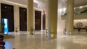 En rummelig lobby med marmorgulv, høje søjler og en moderne lysekrone.
