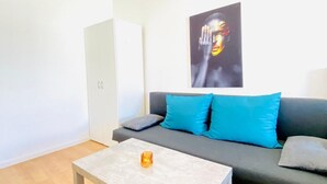 A modern living room with a grey sofa, blue cushions, a white cabinet, and a small table with a candle. - Cozy Stay in Shared Apt  Short Walk to Westbahnhof (Vienna)