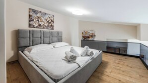Un dormitorio moderno con una cama tapizada en gris, ropa de cama blanca y un cuadro sobre ella.