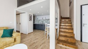 Un apartamento moderno con escalera de madera, una cocina con encimeras de mármol y una sala de estar con sofá y cojín verde.