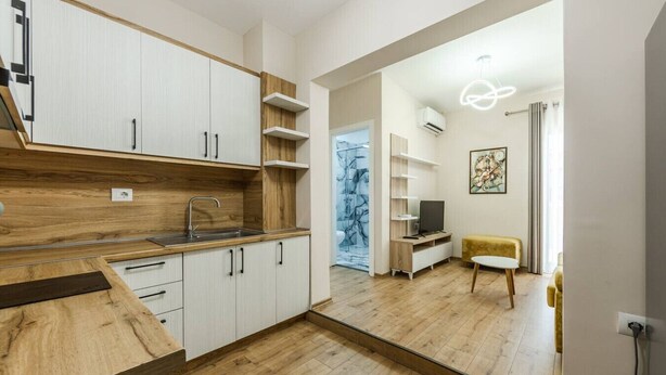 A modern kitchen with wooden cabinets, a built-in sink, and a dining area with a yellow chair and a TV. - Luma One-bedroom Penthouses by Kondo Stays (Tiranë)