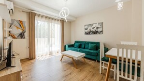 A modern living room with a teal sofa, a white coffee table, and a dining area with a white table and chairs. - Luma One-bedroom Penthouses by Kondo Stays (Tiranë)