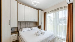 A bedroom with a bed, wooden wardrobe, and a window with curtains. - Luma One-bedroom Penthouses by Kondo Stays (Tiranë)