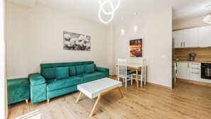 A modern living space with a teal sofa, a white coffee table, and a dining area with a white table and chairs. There is a kitchen with white cabinets and a wooden countertop. - Luma One-bedroom Penthouses by Kondo Stays (Tiranë)