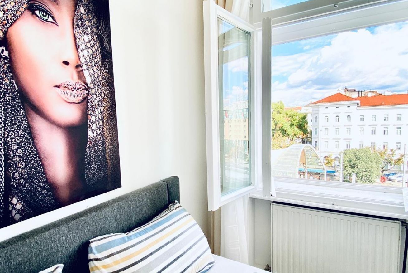 Een slaapkamer met een bed, een raam met uitzicht op gebouwen, en een poster aan de muur.