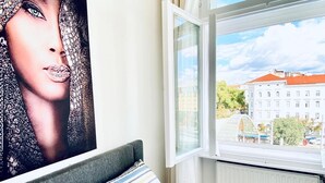 Ein Schlafzimmer mit einem Bett, einem Fenster mit Blick auf Gebäude und einem Poster an der Wand.