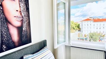 Een slaapkamer met een bed, een raam met uitzicht op gebouwen, en een poster aan de muur.