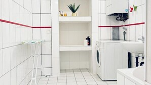 Une salle de bain moderne avec des carreaux blancs, un lave-linge, un évier et une étagère contenant des articles de toilette.