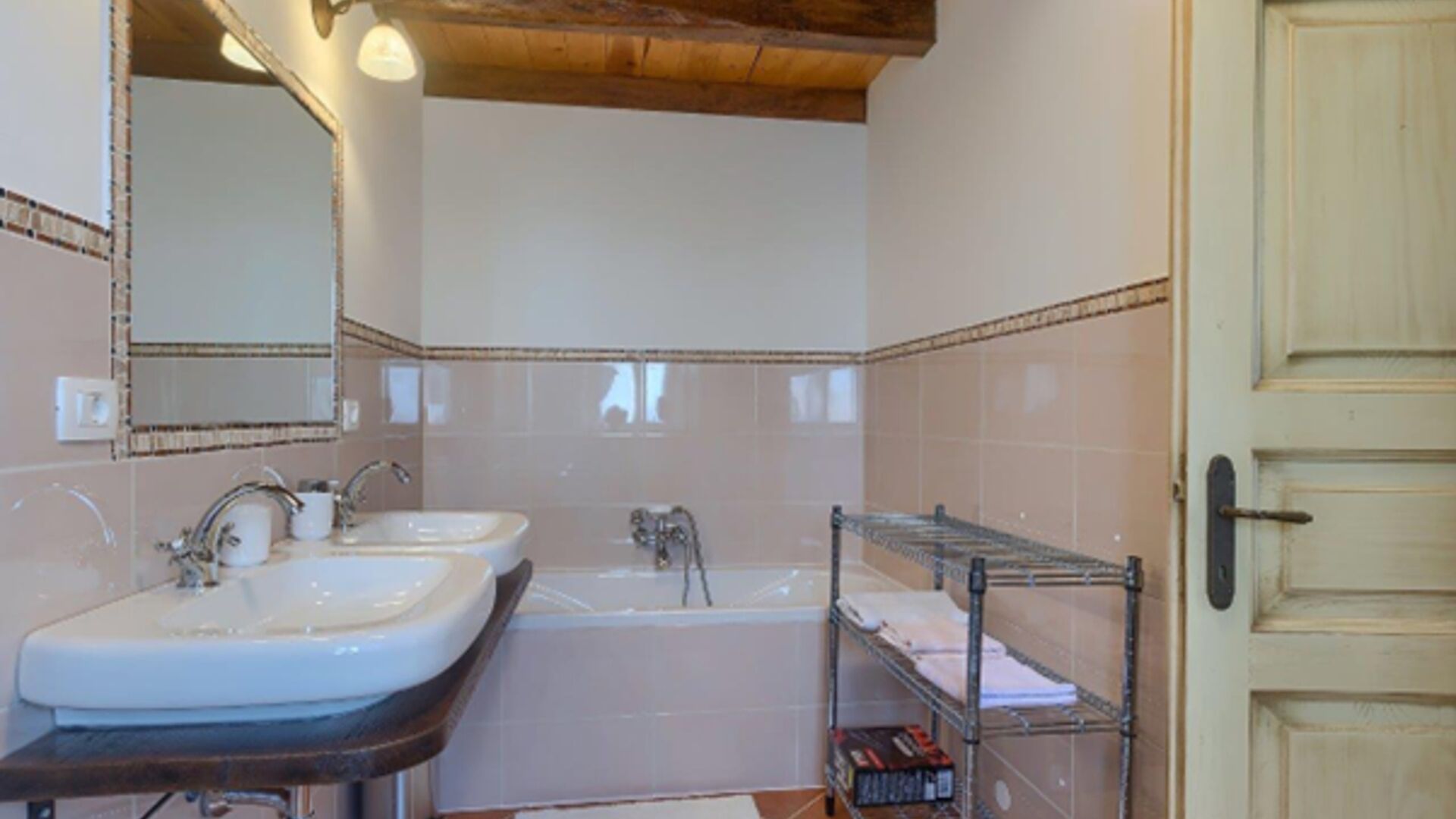 A bathroom with two sinks, a bathtub, and a shelf with towels.