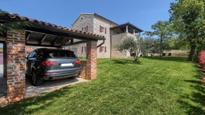 Une maison avec une voiture garée dans un garage fermé, une pelouse bien entretenue et un b âtiment en pierre en arrière-plan.
