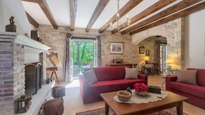A cozy living room with a fireplace, red sofas, a wooden coffee table, and a stone wall.