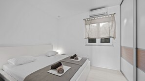 A modern bedroom with a large bed, two bedside tables, a window with a curtain, and an air conditioning unit.