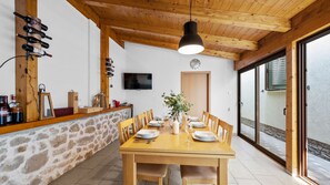 A dining area with a wooden table set for six, a stone wall, and a wooden ceiling.